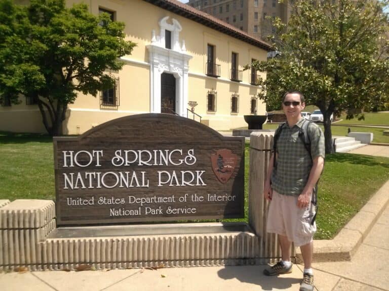 A man stands in front of the Hot Springs National Park sign on Bathhouse Row, the best place to begin one day at Hot Springs National Park Arkansas.