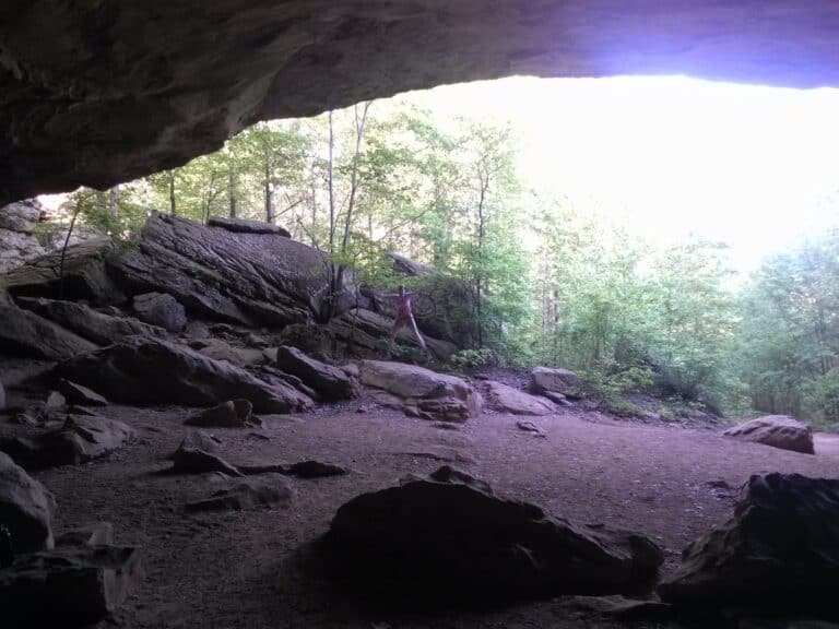 A woman jumps into the air under Rock House Cave in Petit Jean State Park which highlights the expansive cave roof of this park highlight.