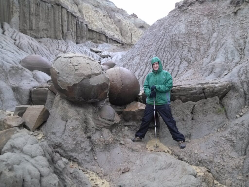 Man standing next to large round rock formations known as Cannonball Concretions in Theodore Roosevelt National Park North Unit.