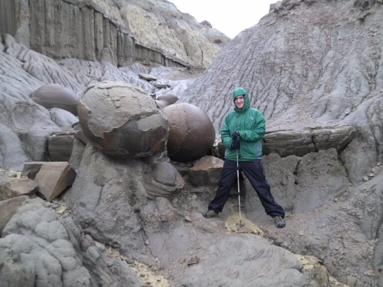 Man standing next to large round rock formations known as Cannonball Concretions in Theodore Roosevelt National Park North Unit.