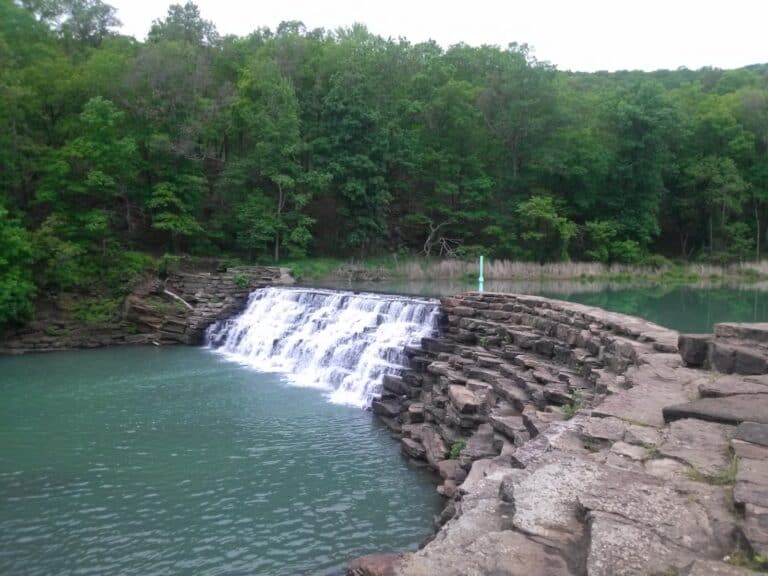 Water flows over the Devil's Den State Park CCC dam from Devil's Lake into bright blue Lee Creek.