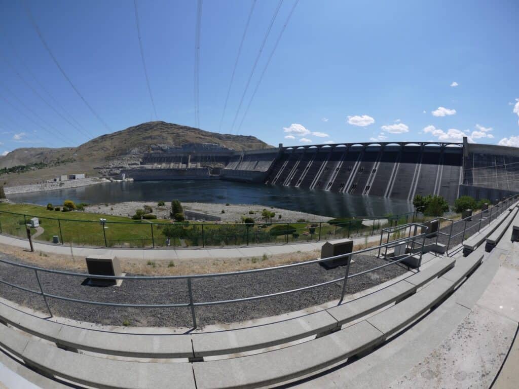 Grand Coulee Dam Washington as seen from the right side and below with a pool of water at the bottom and power lines overhead.