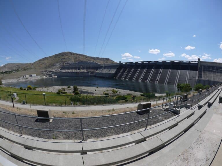Grand Coulee Dam Washington as seen from the right side and below with a pool of water at the bottom and power lines overhead.