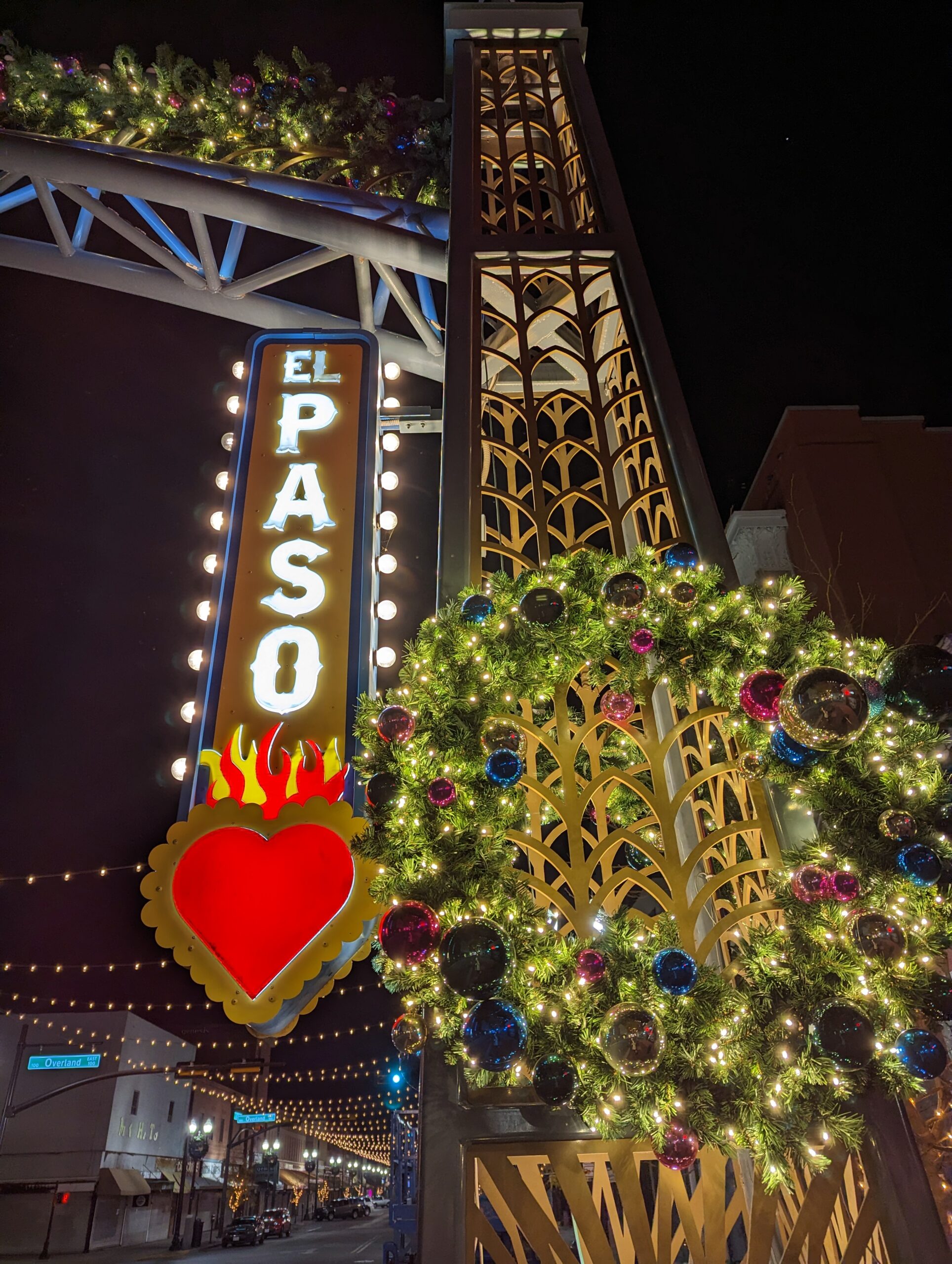 El Paso Texas sign with flaming heart at bottom next to an illuminated Christmas wreath.