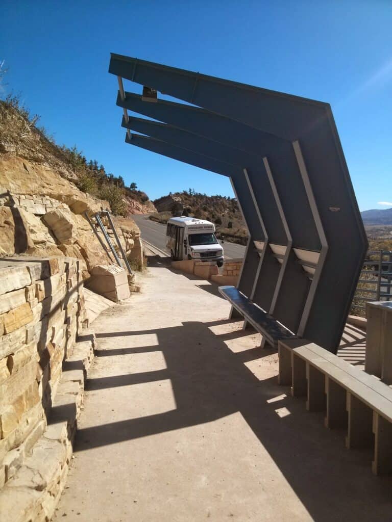 A shuttle tour bus drives the paved road up Dinosaur Ridge in Colorado, stopping at an exhibit with dinosaur footprints.