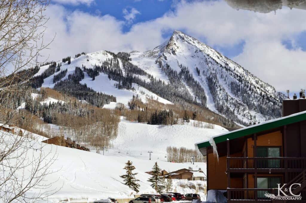 Mount Crested Butte dominates the landscape, covered in snow. A lodge with icicles along the roofline sites in the foreground.