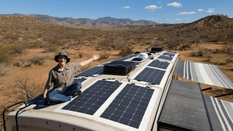 Man sitting on roof off RV gesturing with one arm over the installed RV solar system.