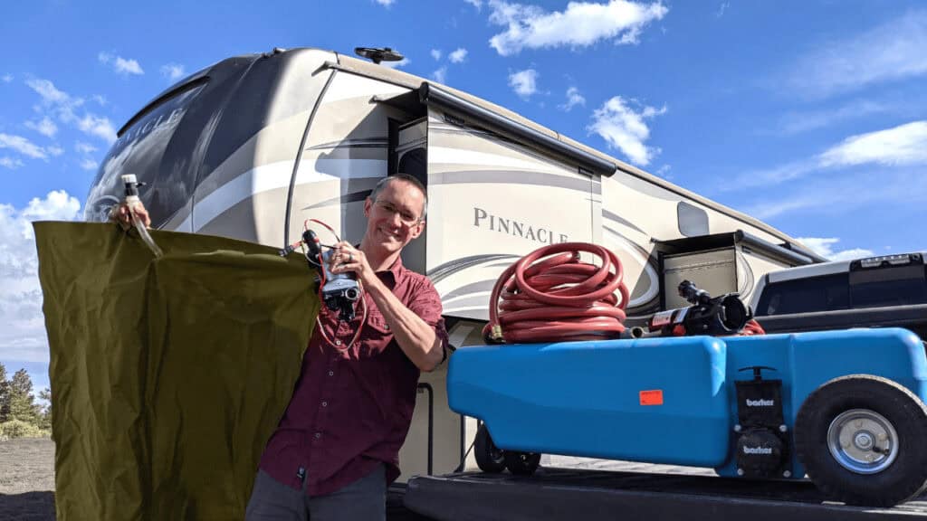 Man holding a water bladder standing next to a portable waste tank, great tools to make RV boondocking easier.