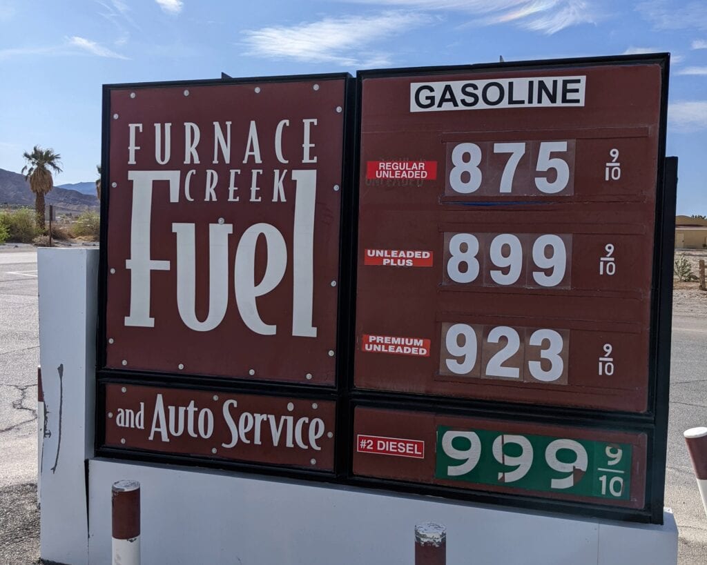 Gas station sign at Furnace Creek in Death Valley National Park shows extremely high fuel prices: .75 for regular, .99 for plus, .23 for premium, and .99 for diesel. A helpful reminder for families visiting the park to fuel up before arrival.