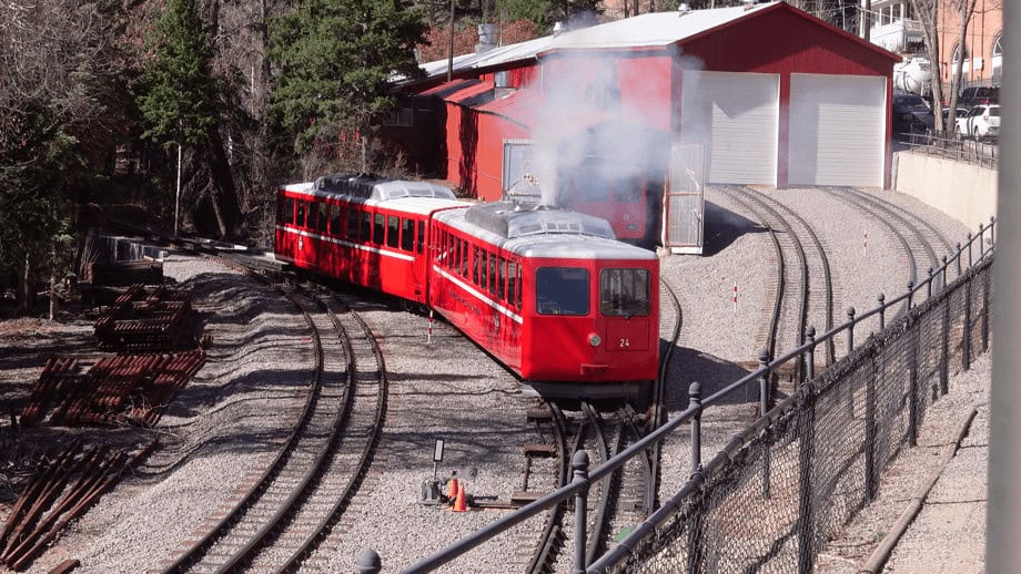 The red cog railway engine and cars leaves the station to head up Pikes Peak.