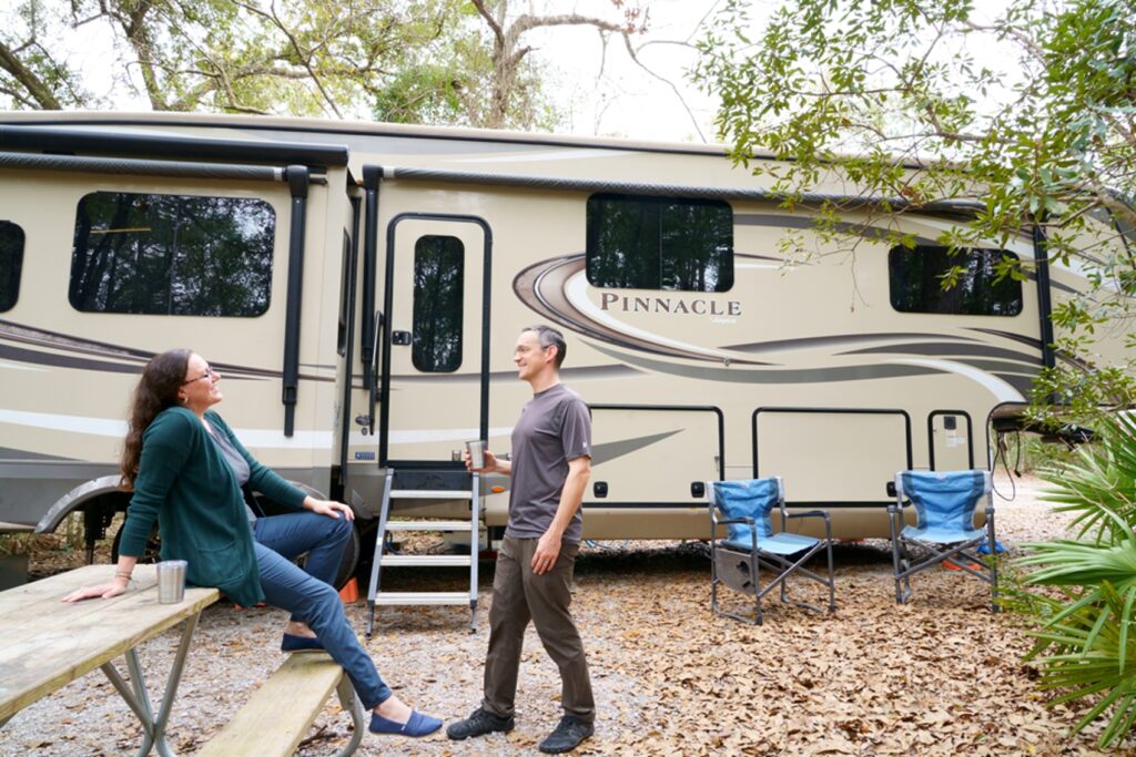 Woman sitting on picnic table with man in front of RV both wearing KUHL travel pants