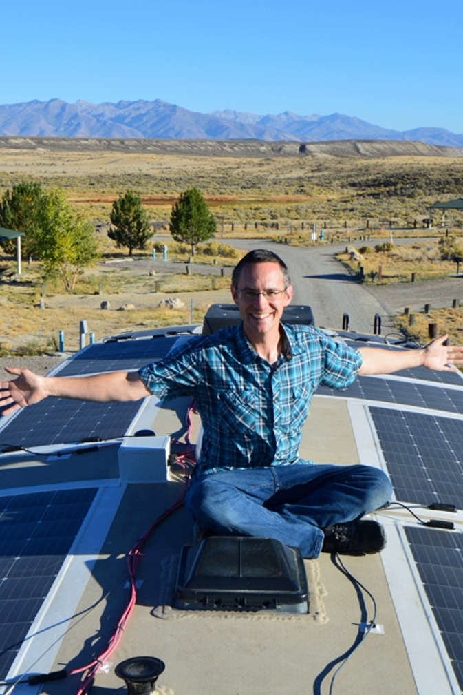 Man on top of RV roof showing solar setup