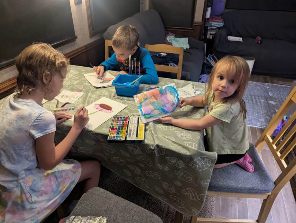 Three kids sit at a table and do artwork with homeschool family travel resources